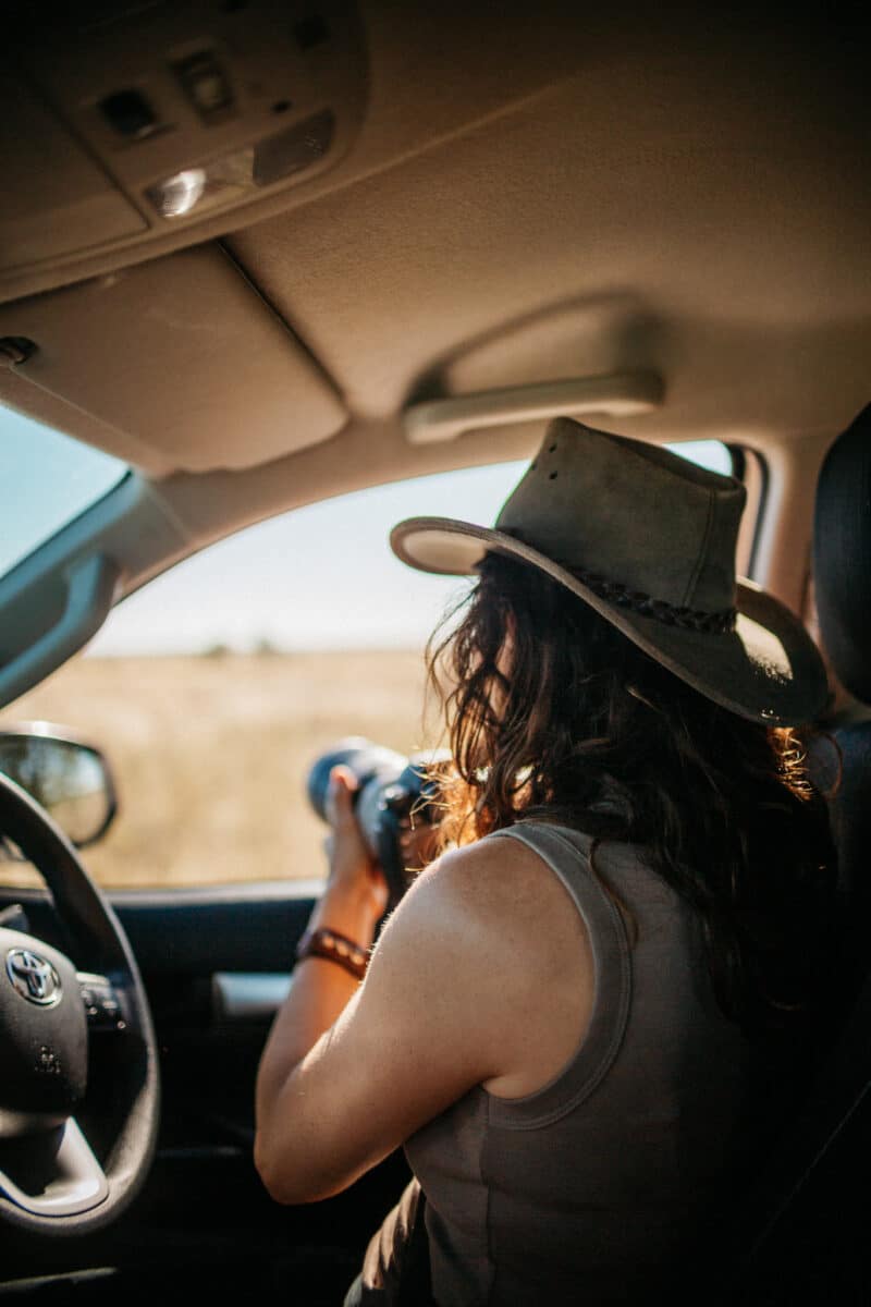 Femme au chapeau photographiant depuis l'habitacle du 4×4